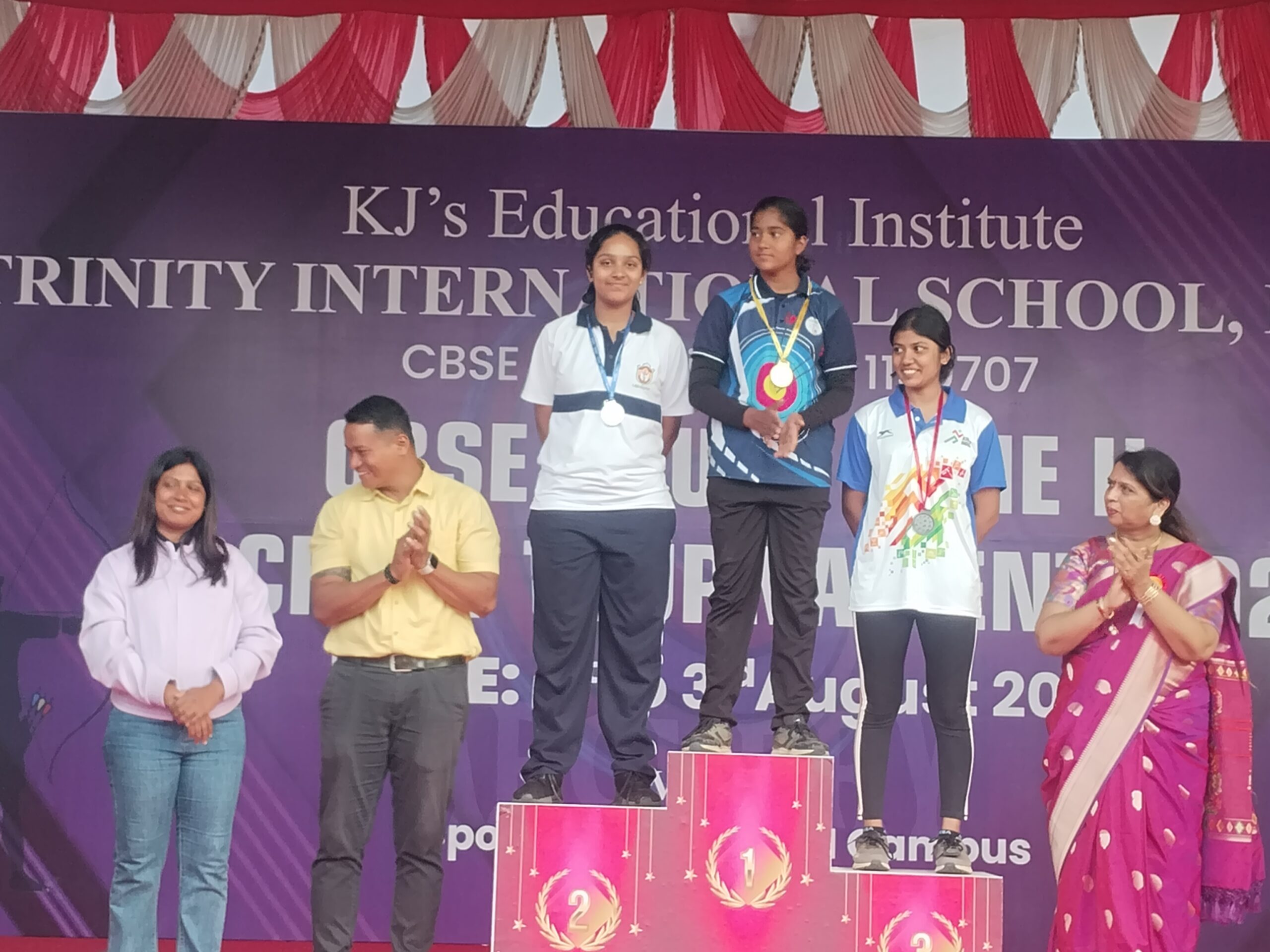 A young female archer, possibly Jidniyasa Bharambe, holding a gold medal and a bow, smiling proudly. The image should convey achievement and the sport of archery.